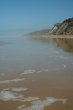 Tranquil Beach Landscape with Wet Sand, Sea Foam, and Blue Sky