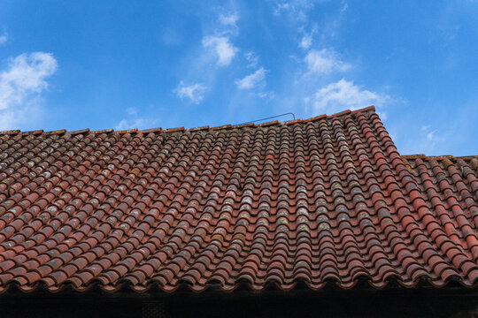 Weathered beauty: close-up of aged terracotta roof tiles on a sagging gable. Patina of lichen, dirt, and time creates a unique texture against the sky. Ideal for material studies, historical themes