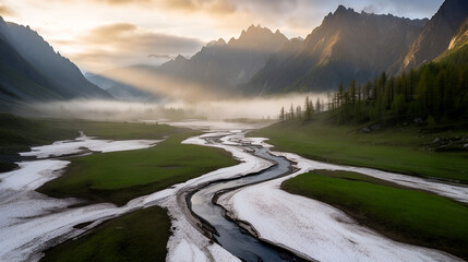 Aerial panoramic spring alpine valley with meandering stream, melting snow and misty conifer peaks at sunrise