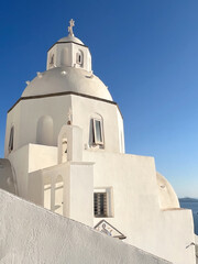 Fototapeta premium White washed church showcasing traditional cycladic architecture with a prominent dome and cross, set against a vibrant blue sky on a greek island, representing travel and tourism