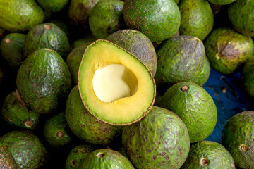 Fresh, ripe avocado cut in half on a pile of avocados. Healthy food, organic produce, tropical fruit, natural market concept, vibrant green texture, exposed pit, farm-to-table freshness.