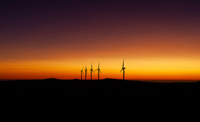 Obraz premium Wind turbines generating green energy at sunset in Madeira, Portugal. Mountain landscape with sustainable technology. Renewable energy in a rural countryside setting.