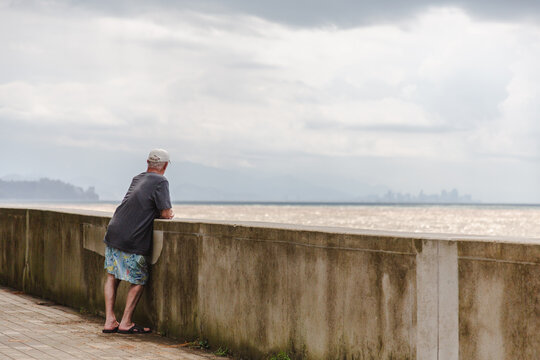 Kobuleti, Georgia - 21 August 2025: View of a solitary man gazes out over the shimmering Black Sea from the weathered promenade, lost in contemplation beneath a sky heavy with brooding clouds.