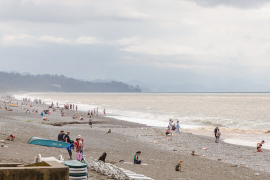 Kobuleti, Georgia - 21 August 2025: View of a pebbly beach with scattered people enjoying the day, the sea reflecting a muted sky, and distant mountains fading into the horizon.