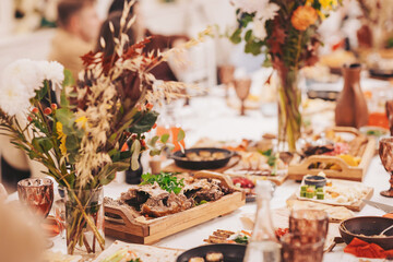 Dinner table set with various dishes, drinks, and flowers in a gathering space during an evening event with friends and family celebrating together