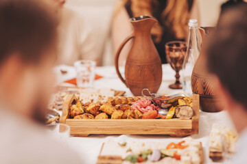 Gathering around a table with a wooden tray of food, traditional drinks, and people enjoying a meal in a cozy setting during an evening event