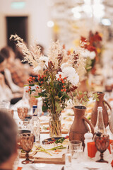 Gathering of friends at a dining table with flowers and dishes during a celebration event in a decorated hall setting