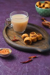Salty Indian cookies bhakar badi with chickpea flour and spices filling with a cup of masala tea on a wooden tray against a purple concrete background.