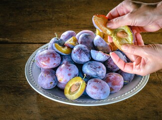 A person is preparing to eat a freshly picked plum. The fruit is halved, exposing its pit and...