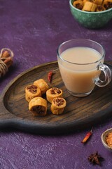 Salty Indian cookies bhakar badi with chickpea flour and spices filling with a cup of masala tea on a wooden tray against a purple concrete background.
