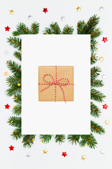 Christmas, New Year vertical holiday layout. Christmas gift in craft paper in frame of fir tree branches and decorations on white flat lay background. Perfect for holiday greetings, banners, social