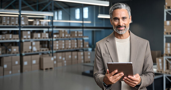 Warehouse manager holding tablet standing near cardboard boxes background. Logistic commercial storage retail goods supply. Storehouse distribution, industrial merchandise and delivery. Banner - Powered by Adobe