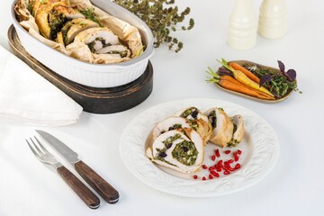 Sliced stuffed chicken is attractively served on a white plate with pomegranate seeds. Roasted carrots, herbs, and thyme add to a lovely display of supper