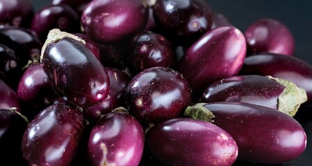 A pile of fresh, glossy eggplants sit together in a cluster, waiting to be cooked. The dark purple skin shines under the light