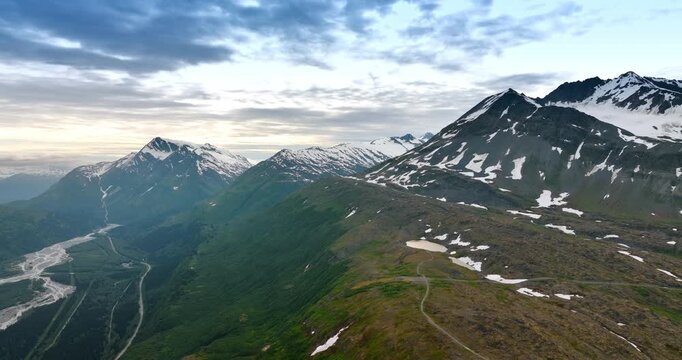 Panoramic View of Mountain Ridge Over Alaskan River Valley. A sweeping vista shows a rocky, dark mountain ridge covered in patches of snow and green growth