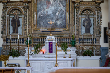altarpiece in a historic italian church with gilded details, two saint statues, a gold crucifix, and a purple liturgical stole on the marble altar