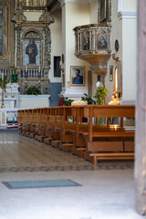 empty church interior showing rows of wooden pews, a decorative gilded altar with a saint's image, a pulpit, and glowing candlelight creating a peaceful, spiritual atmosphere