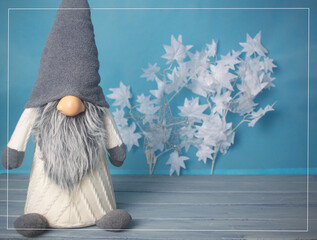 Image of a Christmas gnome on a blue background, with white leaves to the right,