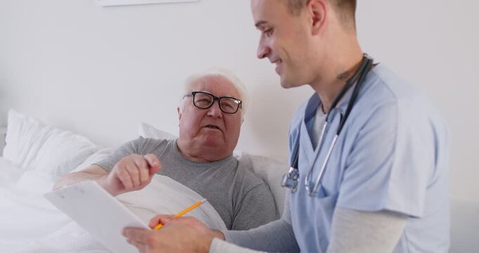Doctor or caregiver engages in a conversation with a senior man patient at a nursing home. They discuss healthcare, care treatment, and the patient well-being during time at the facility.