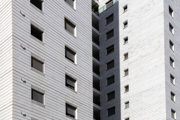 Close up view of a modern residential highrise facade with white cladding square windows and deep shadows. Minimal urban architecture texture and geometry in bright daylight