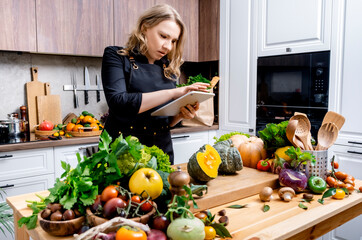 Home cook preparing pumpkin in bright modern kitchen, checking recipe on tablet and arranging fresh vegetables on wooden counter during autumn day. Healthy eating, seasonal cooking