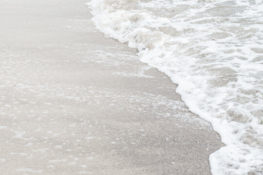 A tranquil coastal scene where smooth sand meets foamy shoreline as gentle waves roll in.Perfect for themes of relaxation, nature, vacation.Demonstrating trendy white color of 2026 year - cloud dancer