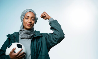 Muslim female athlete flexing bicep holding soccer ball, showing confidence and strength, achieving goals in sport and empowerment