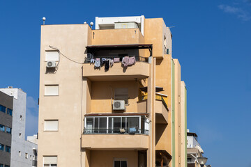  Israeli residential building with stacked balconies hanging laundry air conditioners and a stucco facade under bright blue sky. Mediterranean urban housing scene and everyday city life.