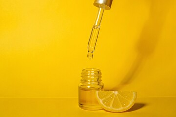 Dropper with oil and lemon slice. Glass dropper releasing clear oil or serum above small bottle beside a lemon slice on a bright yellow surface, clean skincare aesthetic with citrus freshness.