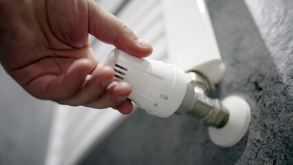 Hand adjusting a white radiator valve in a modern home, showcasing the heating system's functionality and the importance of temperature control in comfortable living spaces