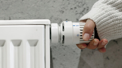 Hand adjusting a white radiator thermostat, showcasing warmth control in a modern home environment, emphasizing comfort and energy efficiency in daily living
