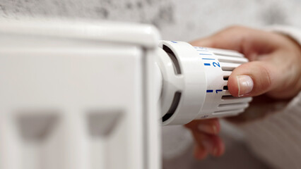 Hand adjusting a white radiator thermostat control in a cozy indoor setting, showcasing home...