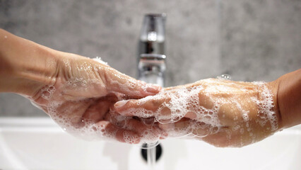 Two hands covered in soap bubbles are gently washing each other under a modern faucet, highlighting the importance of hygiene and cleanliness in daily routines