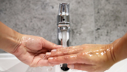 Two hands under running water from a modern faucet, showcasing the importance of hygiene and cleanliness in daily routines, emphasizing health and wellness practices