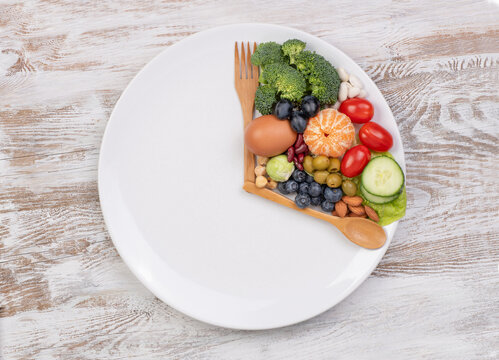 Intermittent fasting concept, spoon and fork on a white plate with food looking like a clock, top view