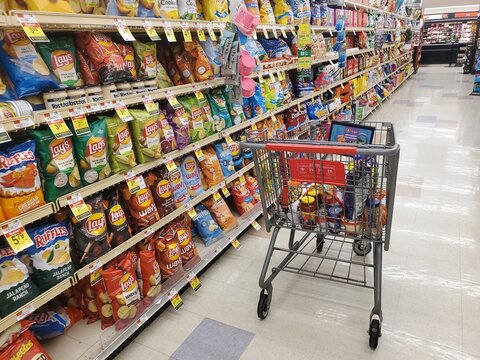 Wilmington, Delaware, U.S - Dec 2, 2025 - The grocery aisle stocked with popular chips of Lay&rsquo;s, Doritos, Ruffles, Tostitos in bright packaging, price tags, next to a full shopping cart.
