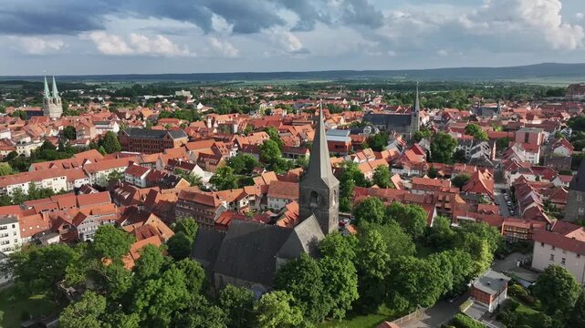 Drone flies in a semicircle to the right around a church, looking toward Quedlinburg&rsquo;s old town and marketplace, under a dramatic pre-storm sky, Saxony-Anhalt.