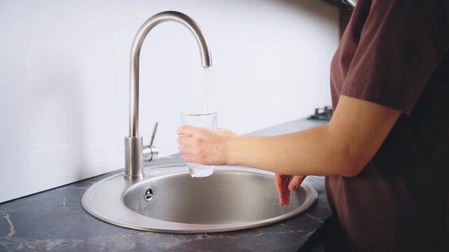 close-up shot person hand woman using faucet opening tap with clean water filling full glass, closing turns off chrome plated tap. Clear water running. Using nature eco resource trendy kitchen room