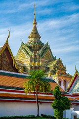 Fototapeta premium Exterior view of Wat Pho with richly decorated stupas covered in colorful floral ceramics and golden temple roofs shining under a clear blue sky on a bright sunny day in Bangkok.