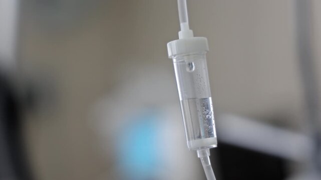 Close up of intravenous drip with saline solution in the hospital room, medical treatment of a sick patient during emergency surgery or therapy