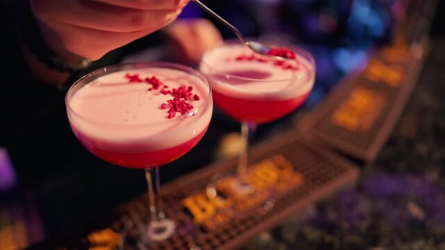 Close proximity view of raspberry decorated fluffy pink cocktails in warmly lit lounge environment