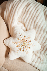 Soft white star-shaped pillow with golden embroidery placed on a fluffy textured blanket.