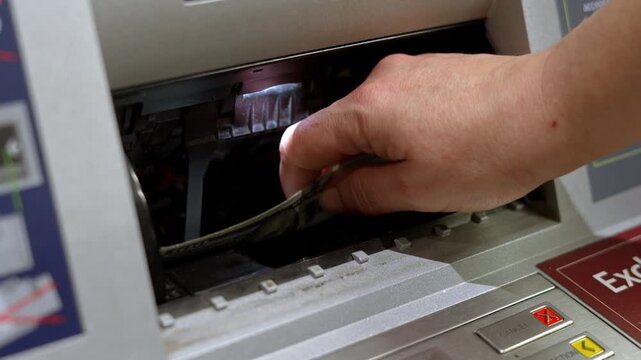 Close-up of hand retrieving US hundred dollar bills from ATM cash dispenser slot. Dollars Retrieved From Cash Slot. ATM Dispenser Releasing Banknotes