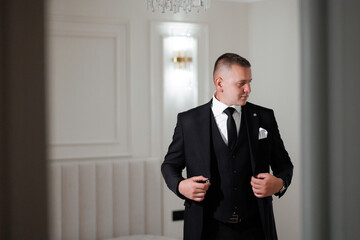 Man adjusting his suit in a bright, elegant room before a formal event