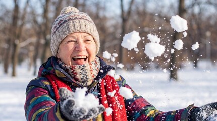 Fototapeta premium Cheerful senior lady throwing snowballs in a winter park, enjoying cold weather. A symbol of active aging and healthy retirement lifestyle for healthcare or holiday concepts.