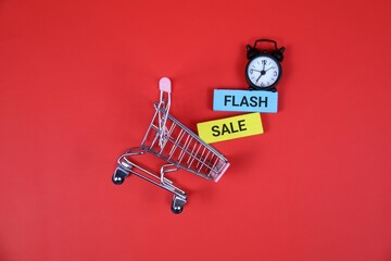A miniature shopping cart sits on a red backdrop beside a small clock and colorful signs reading 'Flash' and 'Sale', conveying urgency, discounts, and quick shopping ideas.