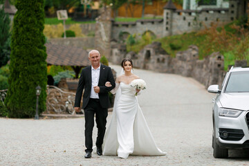 Naklejka premium Bride walks down the path with her father at a beautiful outdoor wedding venue