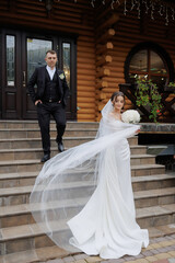 Elegant bride walks down steps as groom waits in front of a rustic lodge during wedding ceremony