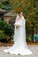 Beautiful bride stands elegantly in garden with bouquet during wedding ceremony