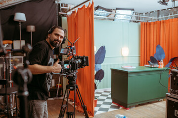 Director of photography with a camera in his hands on the set. Professional videographer at work on filming a movie, commercial or TV series. Filming process indoors, studio